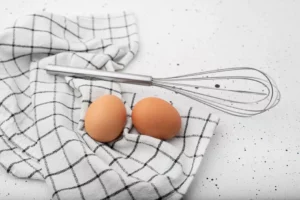 fouet et oeuf sur un torchon pour faire des blancs en neige